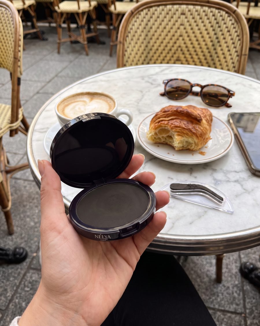 Cutiuța Nélya în nuanța Gri, ținută deasupra unei mese de cafenea